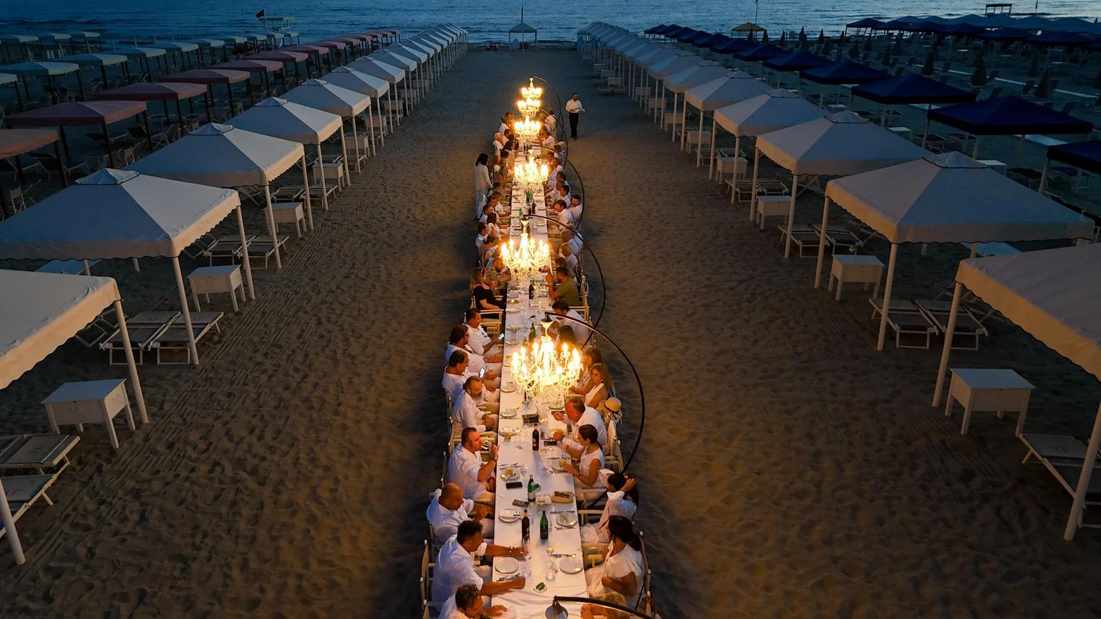 Lunga tavola allestita sulla spiaggia con lampadari
