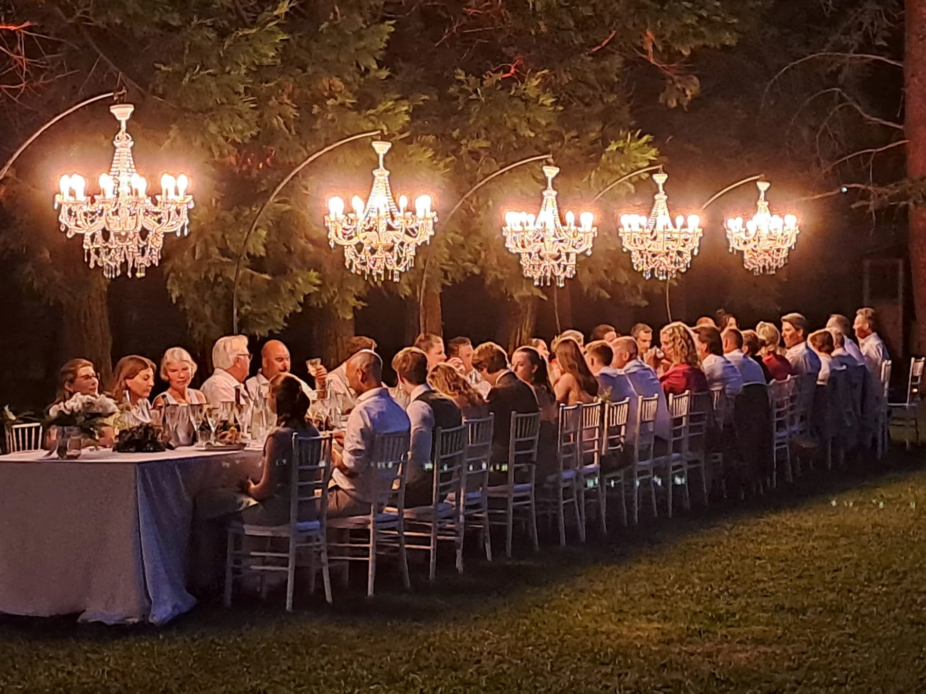 Ospiti a cena sotto lampadari sospesi tra gli alberi